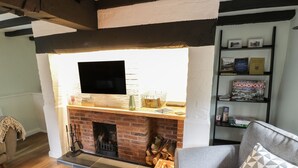 A living room with a fireplace, a flat-screen TV, a bookshelf, and a grey sofa. - 4 Masons Court (Stratford-upon-Avon)