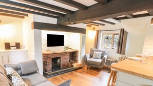 A cozy living area with a fireplace, a sofa, a dining table, and a kitchen counter. - 4 Masons Court (Stratford-upon-Avon)
