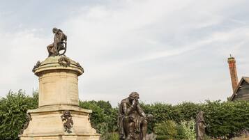 A statue of Hamlet on a pedestal, surrounded by greenery and a brick chimney in the background.