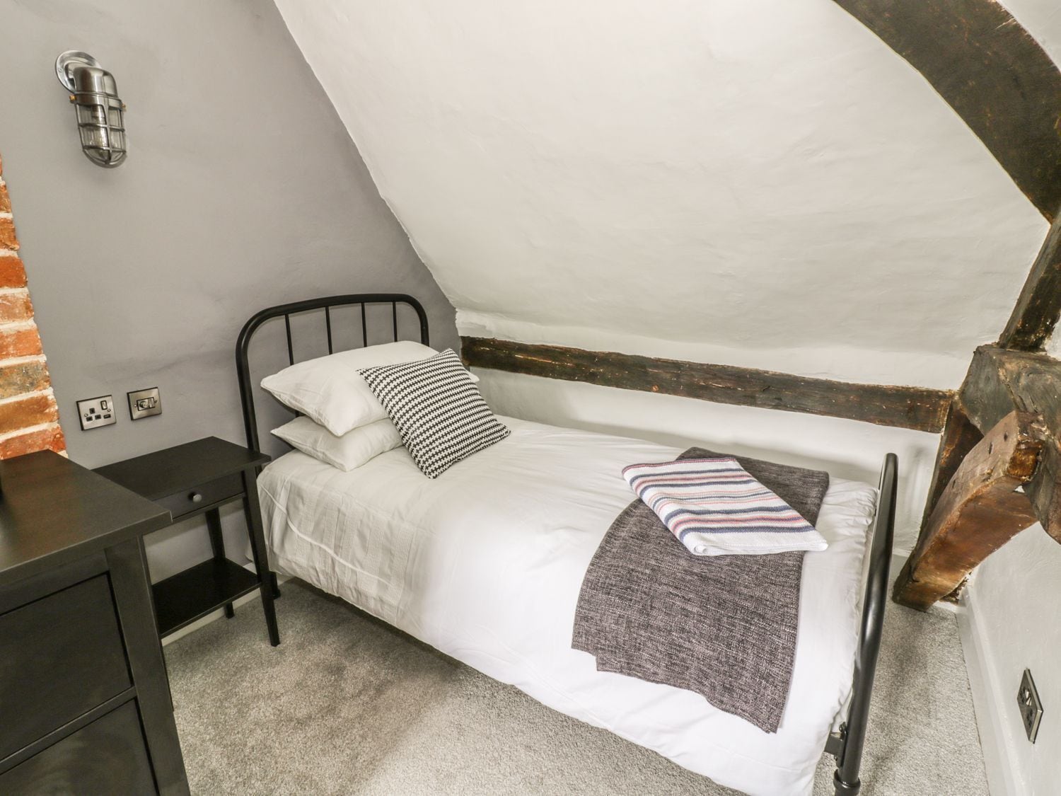 A single bed with a headboard, a bedside table, and a wall-mounted light fixture.