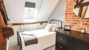 A bedroom with a loft bed, a small window, a brick wall, a wooden beam, a dresser, and a clock. - 4 Masons Court (Stratford-upon-Avon)