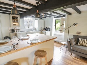 Uma cozinha moderna com uma ilha central, banquetas de madeira, área de jantar com sofá e vista para o verde lá fora.