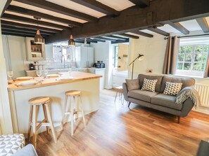 Eine moderne Küche mit einer zentralen Kochinsel, Holzbarhocker und einem grauen Sofa in einem hellen Wohnbereich mit Holzboden.