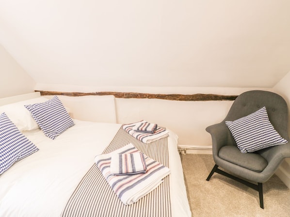 Quarto com cama, cadeira, roupa de cama listrada e almofadas xadrez.