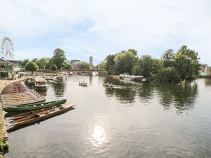 Ein ruhiger Fluss mit anlegenden Booten links, einer Brücke in der Mitte und Bäumen, die das Ufer säumen.
