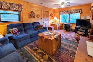 A cozy cabin interior with a sofa, a wooden chest, a television, and a fireplace. - Meadowbrook Log Cabin (Bryson City)