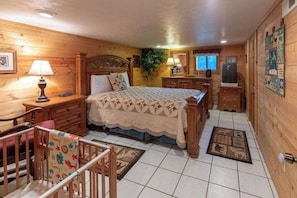 A wooden cabin-style bedroom with a bed, dresser, nightstand, and a crib. - Meadowbrook Log Cabin (Bryson City)