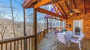 Un patio in legno con tavolo e sedie, una ventola a soffitto e vista sugli alberi.