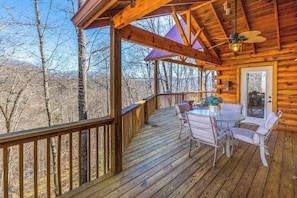 Eine Holzterrasse mit Tisch und Stühlen, einem Deckenventilator und Blick auf Bäume.