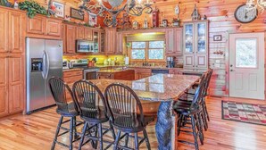 Un'ampia cucina con mobili in legno, una grande isola con sgabelli da bar, un lampadario e un orologio a parete.