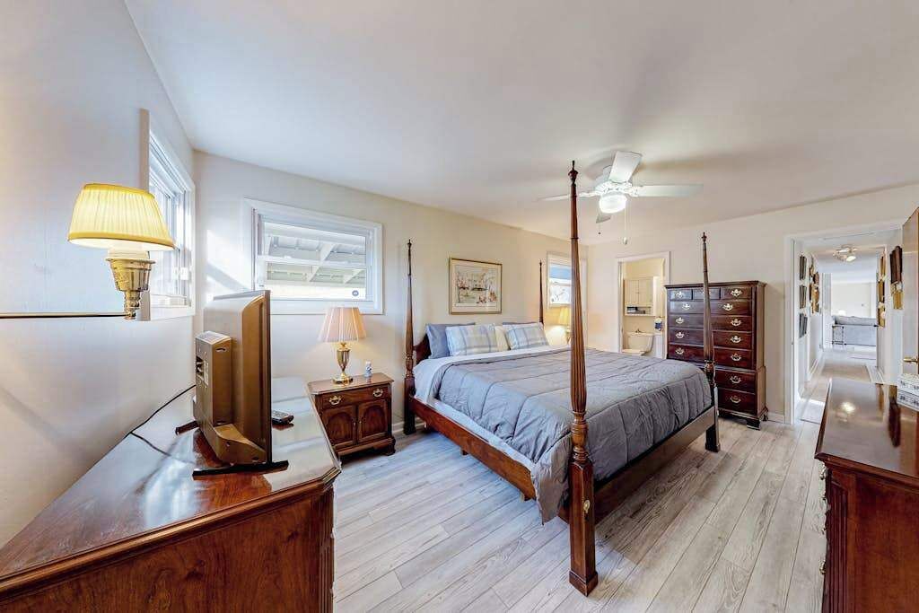A bedroom with a four-poster bed, a television, a dresser, and a ceiling fan.