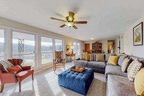 A spacious living room with a ceiling fan, large windows, a sofa set, and a wooden chair. - Sunlit Mountain-View Home w/ Fireplace, WiFi, Alfresco Living & Dining & W/D (Asheville)