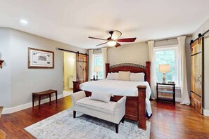 Ein Schlafzimmer mit einem großen Bett, einem Deckenventilator, einer Bank und einem Fenster mit Vorhängen.