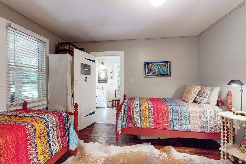 Une chambre avec deux lits, une porte donnant sur une salle de bain et un tableau accroché au mur.