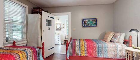 Une chambre avec deux lits, une porte donnant sur une salle de bain et un tableau accroché au mur.