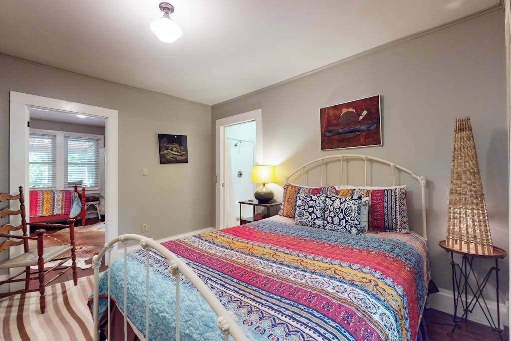 Un dormitorio con cama, una silla, una lámpara y un cuadro en la pared.