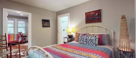 Un dormitorio con cama, una silla, una lámpara y un cuadro en la pared.
