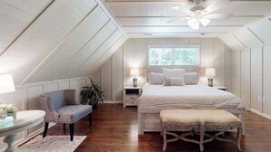A bedroom with a sloped ceiling, a bed with a white bedspread, a chair, a bedside table with a lamp, and a window with blinds. - Expansive Designer Estate w/ TV Room, Spacious Kitchen & Large Yard dog friendly (Arden)