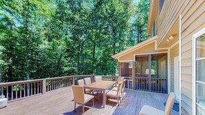 A wooden deck with a table and chairs, surrounded by a railing, and a building with large windows. - Expansive Designer Estate w/ TV Room, Spacious Kitchen & Large Yard dog friendly (Arden)