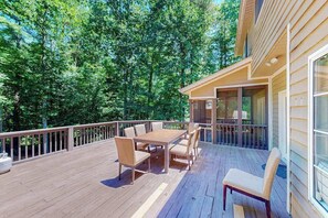 Eine Holzterrasse mit Tisch und Stühlen, umgeben von einem Geländer, und ein Gebäude mit großen Fenstern.