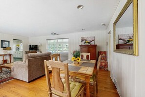 A cozy living room with a sofa, wooden dining table, and chairs. There's a kitchen area with cabinets and a television. - Lovely & inviting home with a sun porch, washer/dryer & AC (Hendersonville)
