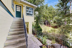 A two-story building with a staircase leading to the entrance, surrounded by lush greenery and trees. - Lovely & inviting home with a sun porch, washer/dryer & AC (Hendersonville)