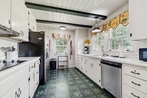 A kitchen with white cabinets, a black refrigerator, a stove, a dishwasher, and a window with a view of greenery.