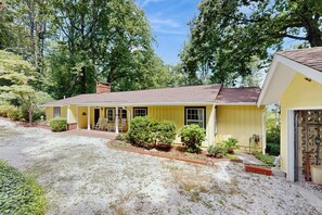 A yellow single-story house with a gravel driveway, a front porch with chairs, and a garage.