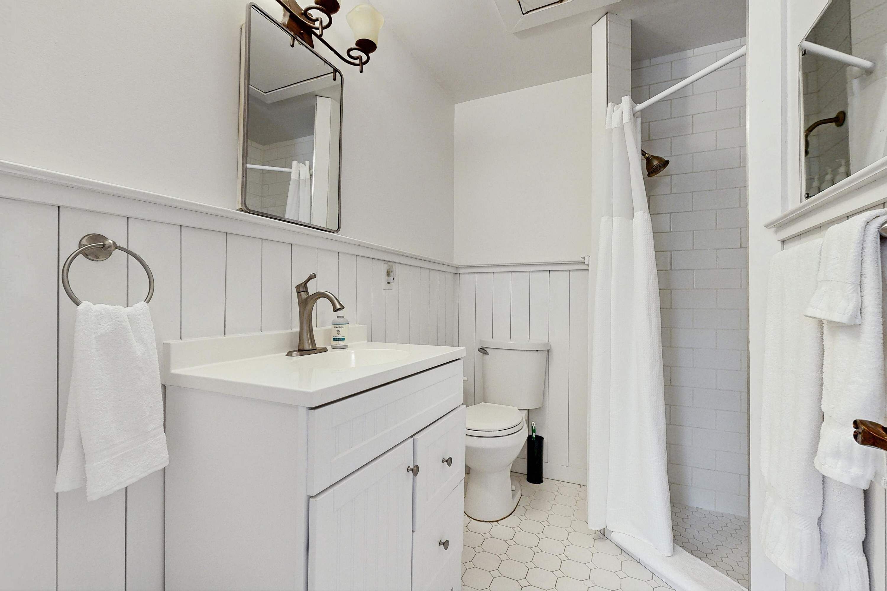 Une salle de bain avec un lavabo, des toilettes et une douche, le tout de couleur blanche.