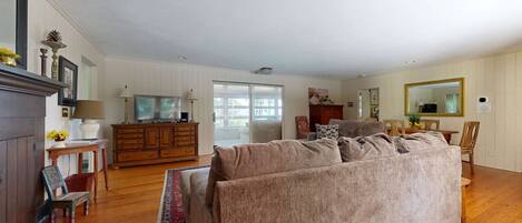 A spacious living room with a large sofa, a television, and a dining area with a table and chairs.