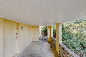 A covered balcony with a yellow wall, a door with a lock, and a view of greenery.