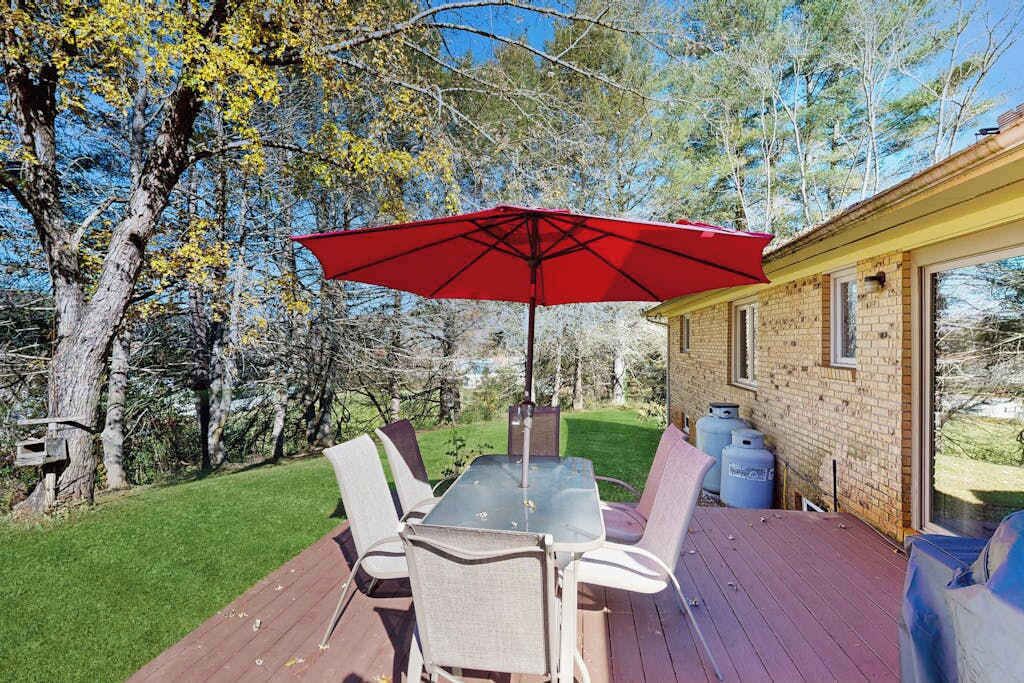 A deck with a table and chairs, a red umbrella, and a brick building in the background.