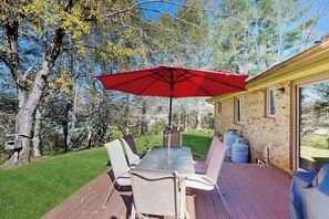 Eine Terrasse mit Tisch und Stühlen, einem roten Sonnenschirm und einem Backsteinhaus im Hintergrund.