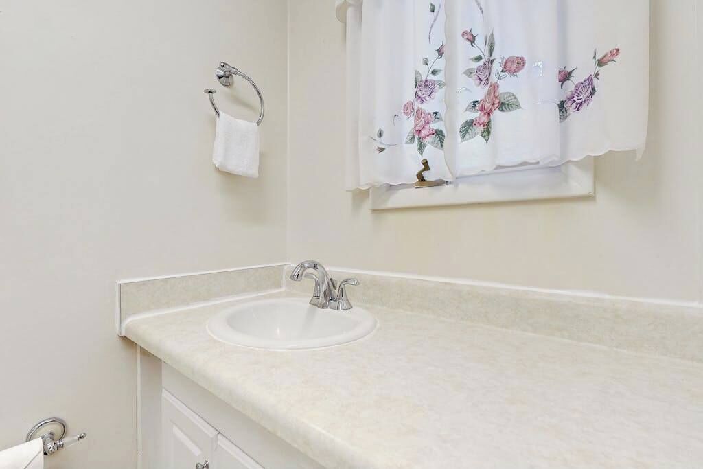 A bathroom with a sink, a towel rack, and a window with floral curtains.