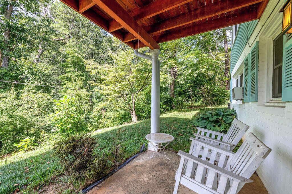 A covered patio with a table and benches, surrounded by lush greenery.