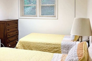 A bedroom with a bed, a nightstand, a lamp, a dresser, and a window with blinds. - Peaceful mountain lake retreat w/free WiFi & private patio, pool (Lake Junaluska)