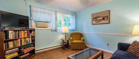 A living room with a bookshelf, a television, a ceiling fan, a window with curtains, a chair, a couch, and a table.