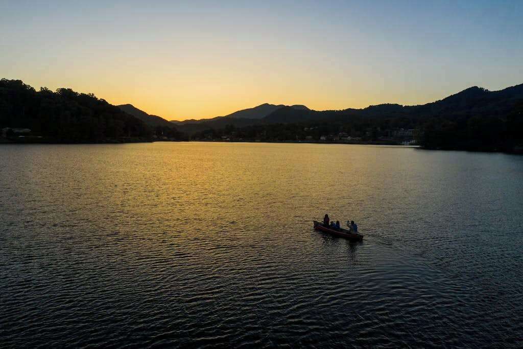 Um lago tranquilo com um barco ao centro, rodeado por colinas e um céu claro.