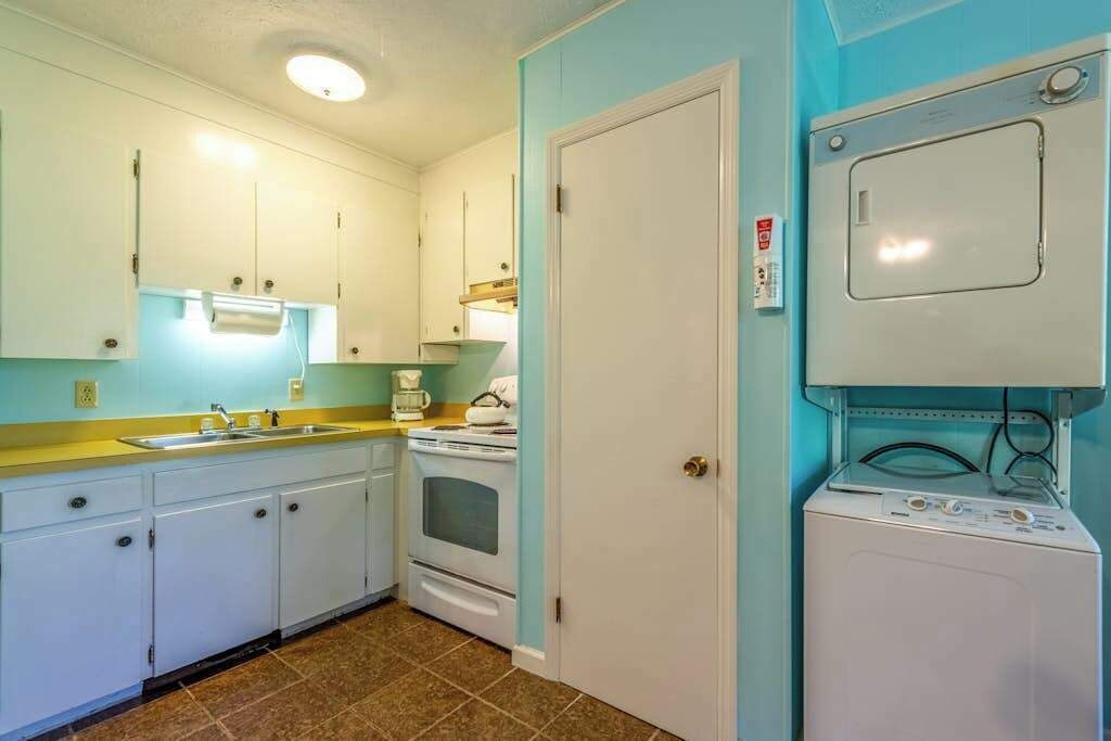 A compact kitchen with white cabinets, a sink, a stove, and a washing machine.