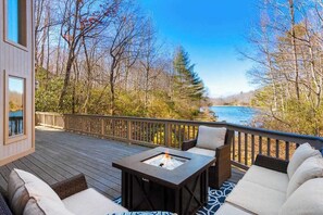 Una terraza con mobiliario exterior, un brasero y vistas a un lago rodeado de árboles.