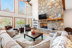 Una sala de estar con chimenea de piedra, un televisor montado en la pared y un ventanal con vistas a una terraza.