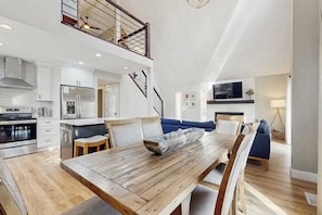 Eine geräumige Küche mit modernen Geräten, ein Essbereich mit Holztisch und ein Wohnbereich mit Sofa und Fernseher.