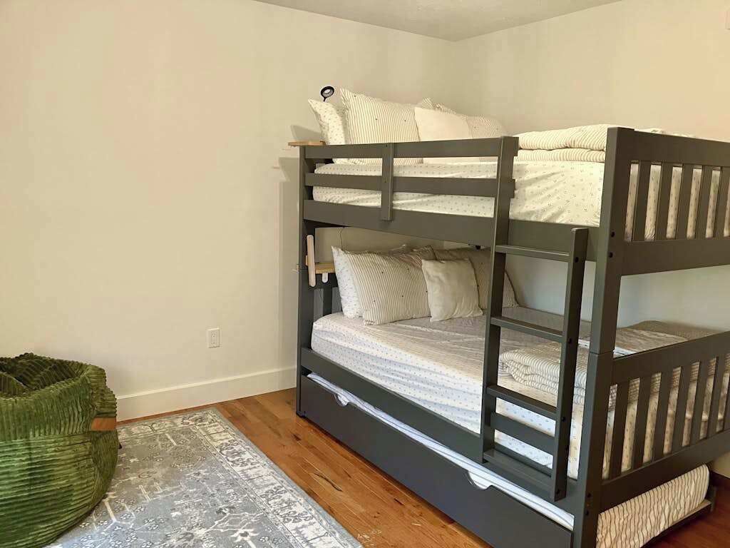 A bunk bed with a wooden frame, a grey floor, and a patterned rug.
