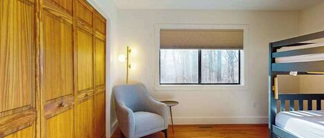 A bedroom with a bunk bed, a chair, a small table, and a window with blinds.