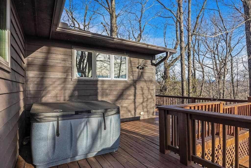 A wooden deck with a hot tub, a window, and a view of trees.