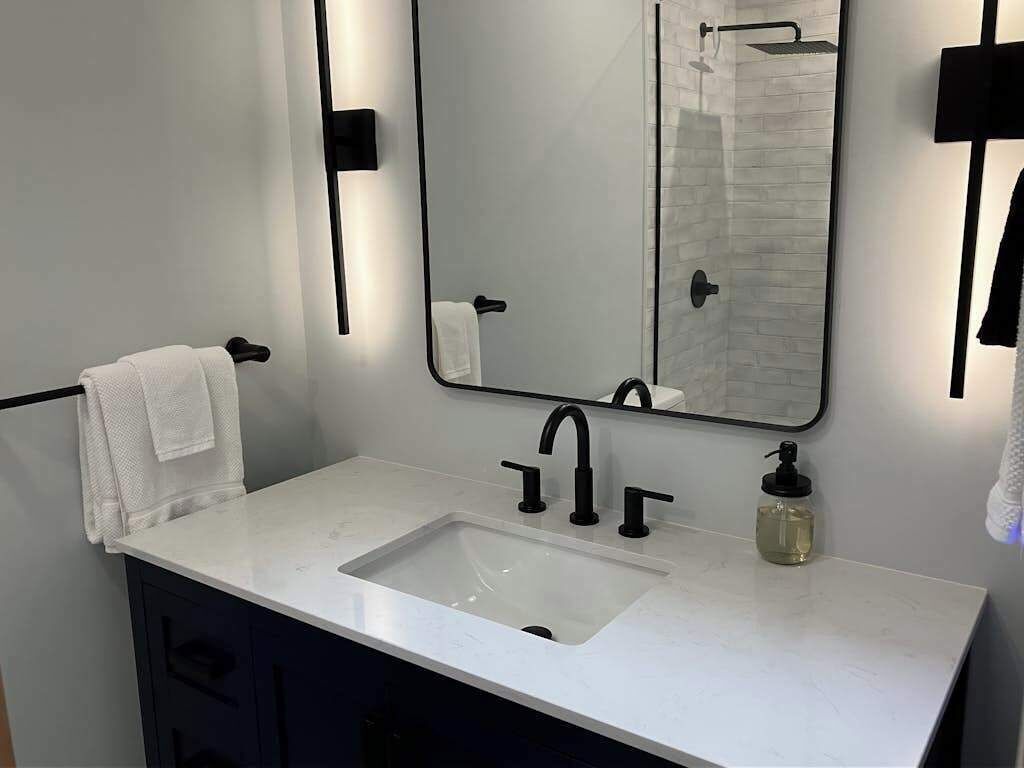 A modern bathroom with a white sink, black faucet, and a large mirror.