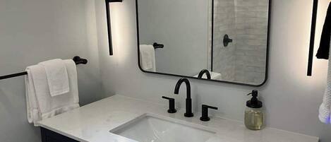 A modern bathroom with a white sink, black faucet, and a large mirror.