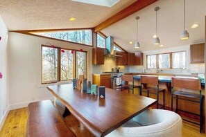 Eine moderne Küche mit Holzausstattung, einem großen Esstisch und Pendelleuchten.