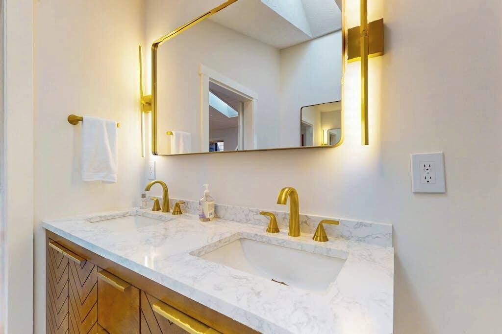 Un baño con lavamanos doble, grifos dorados, un espejo grande y un perchero para toallas.