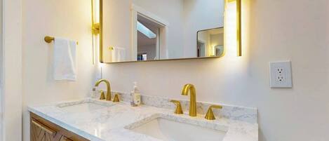 Un baño con lavamanos doble, grifos dorados, un espejo grande y un perchero para toallas.